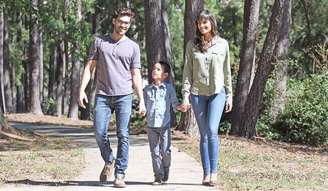 A mother, father, and son walk along a path, holding hands in a park