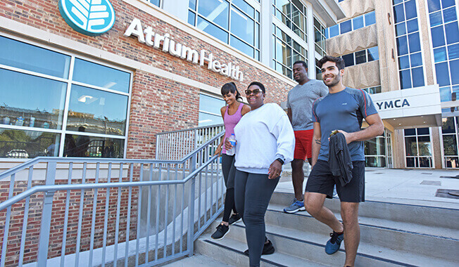 Two men and two women in athletic wear walk down a small set of stairs in front of an Atrium Health YMCA facility