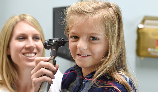 An Atrium Health physician is examining a young blonde girl's ear with an otoscope