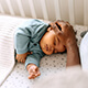 An adult puts their hand on the head of a sleeping baby.
