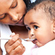 A mother using a spoon to feed her child.