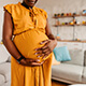 A pregnant woman in a yellow dress holding her stomach.