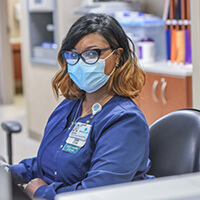 A young nurse wearing scrubs and a face mask.