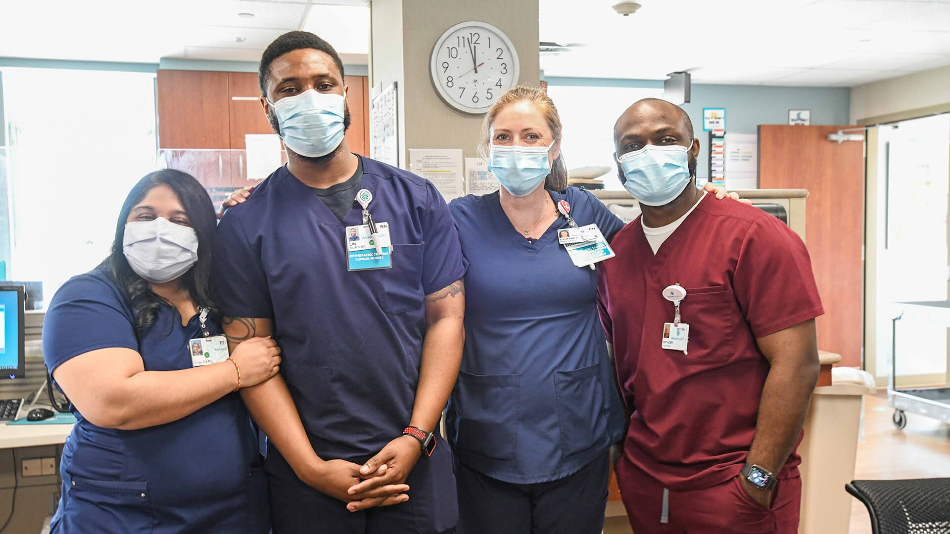A group of nurses and hospital staff wearing masks. Three have blue scrubs and one has red scrubs.