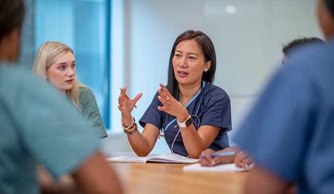 A woman in blue scrubs giving instructions to a class of nursing students also in blue scrubs.