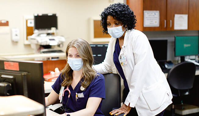 Two medical professionals wearing face masks and looking at a computer.