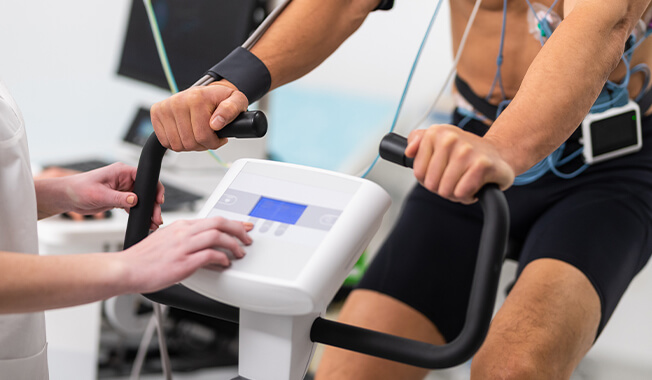 Person riding an exercise bike monitored with medical equipment. 