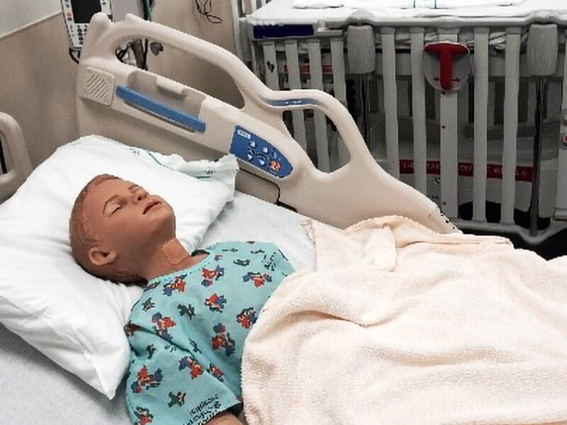 A hospital bed with a patient simulation dummy on it.