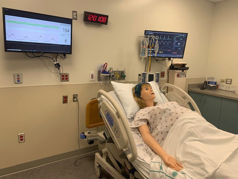A mannequin representation of a patient resting in a hospital bed.