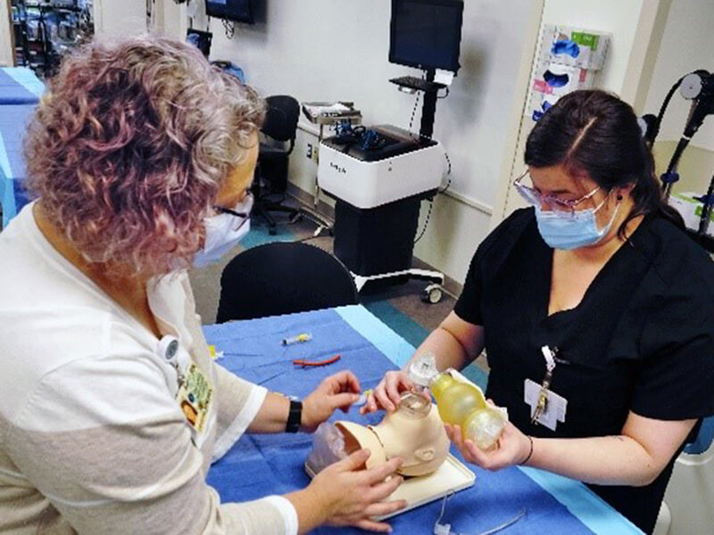 Two women working on a piece of medical equipment while sitting at a table.