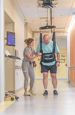 Man standing, assisted by Neurologic Physical Therapists and specialized equipment