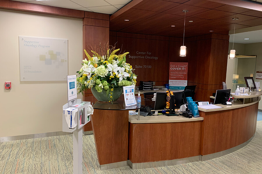 The Center for Supportive Oncology front desk with computers on it and a large potted plant.