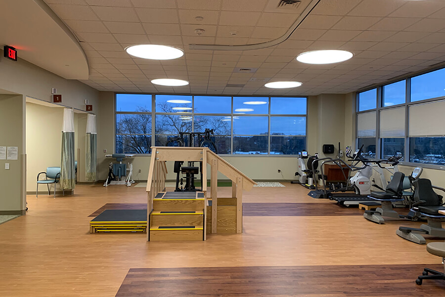 A large physical therapy treatment room with a ramp and several bikes and treadmills.