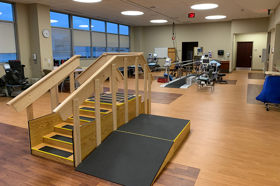 A large physical therapy treatment room with a ramp and several bikes and treadmills.