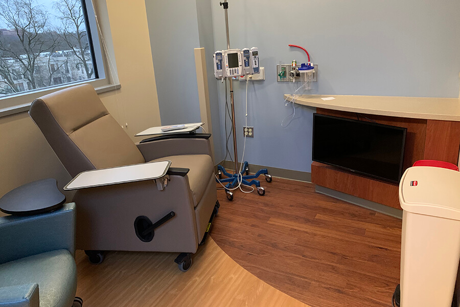 A small doctor's office with a desk, chair and IV drip inside the office.