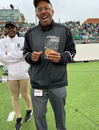 A man in a green and black jacket standing outise and smiling.