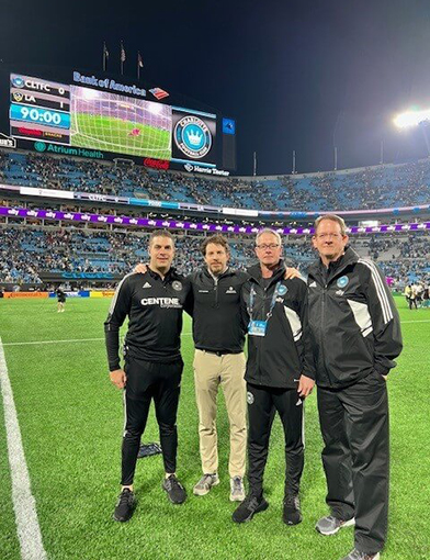4 men in athletic gear standing on the field in a stadium.