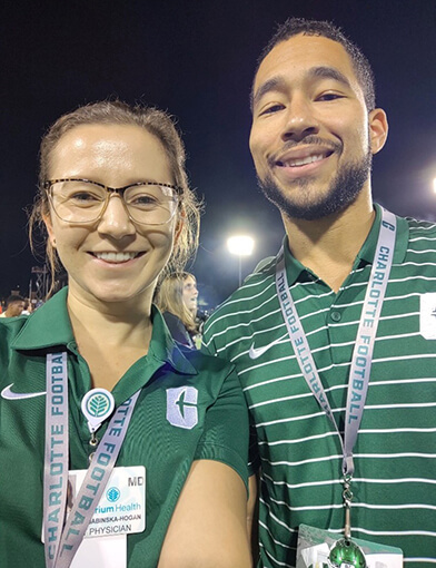 A young man and woman in green shirts smiling and standing together.