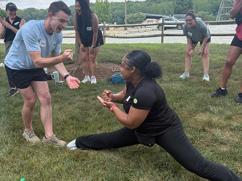 A woman in black clothes doing the splits while several men and women look on.