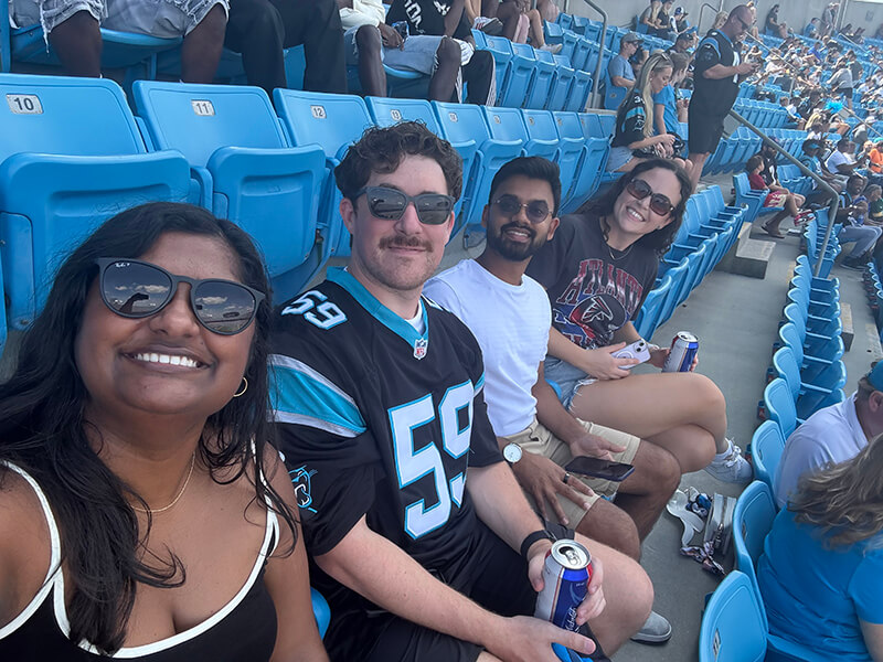 Two men and two women smiling and sitting in the stands for a football game.