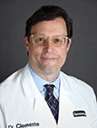 A man wearing a white lab coat sitting in front of a dark background.