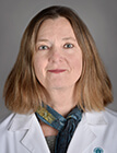 A woman wearing a white lab coat sitting in front of a dark background.