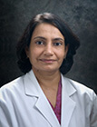 A woman with short hair, wearing a lab coat and sitting in front of a dark background.