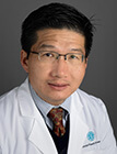 A man wearing a lab coat sitting in front of a dark background.