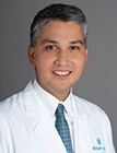 A man wearing a lab coat standing in front of a dark background.