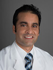 A man wearing a lab coat and a tie smiling at the camera.