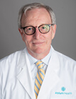 A medical professional with short hair and glasses in a white lab coat.