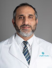 A headshot of a man wearing a lab coat and sitting in front of a dark background.