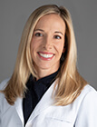 A woman with a lab coat sitting in front of a gray background.