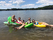 Four people on inflatable rafts and inner tubes on a lake.