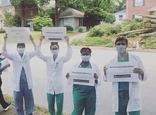 A group of doctors in lab coats outside by a street holding signs.