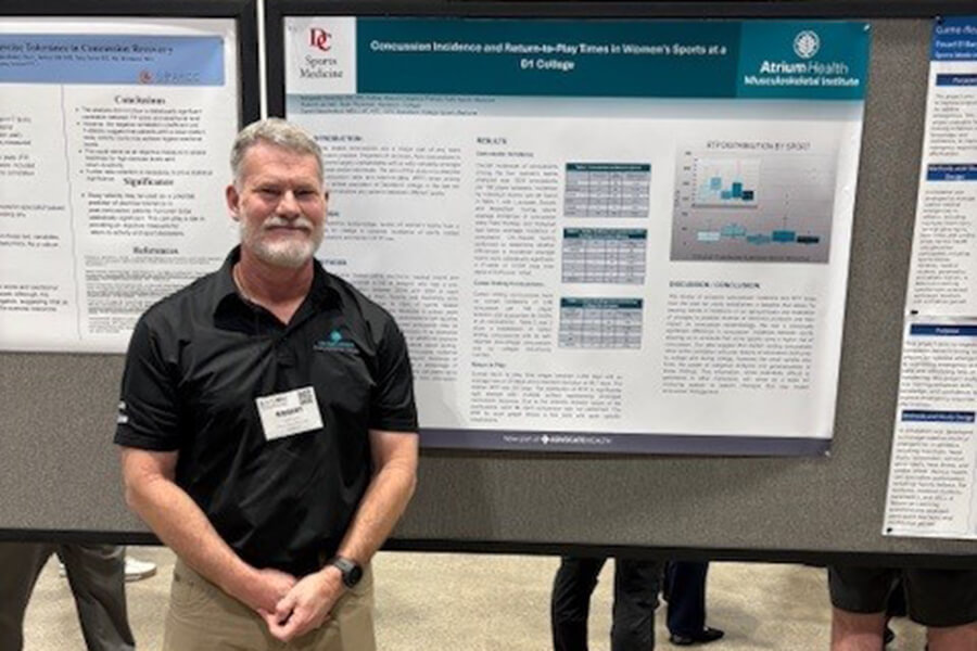 A man in a black polo wearing a lanyard name tag standing next to a chart full of research information.