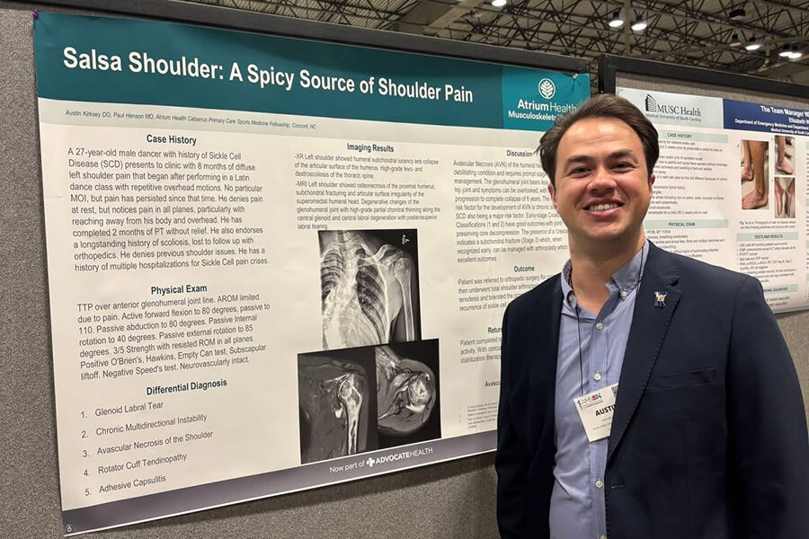 A man in a sports coat wearing a lanyard name tag standing next to a chart full of research information.