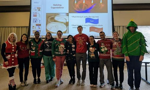 Group of Urology residents wearing Christmas outfits in front of a presentation.