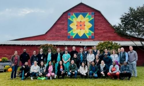 Urology residents in large group of male and female outside of a barn with a painting on the front of it.