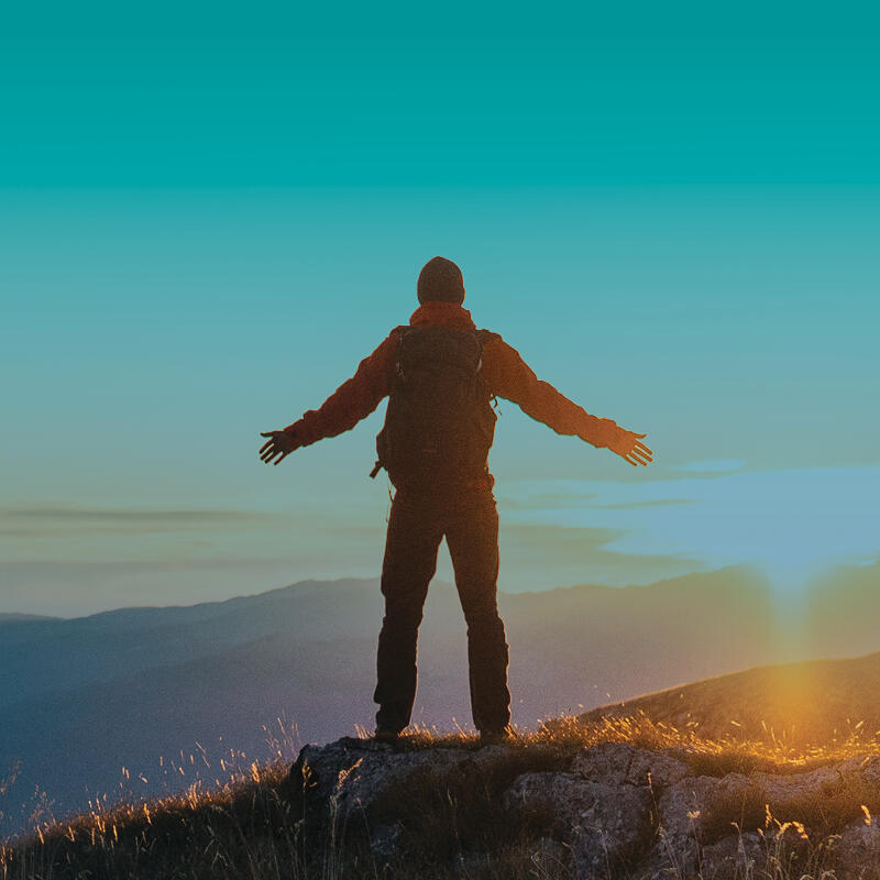 Person standing at the top of a mountain with arms outstretched. 
