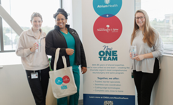 Three women smiling and standing by a banner display.