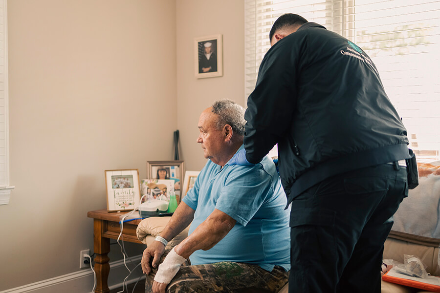 A medical professional checking on an older man sitting his on couch at home.