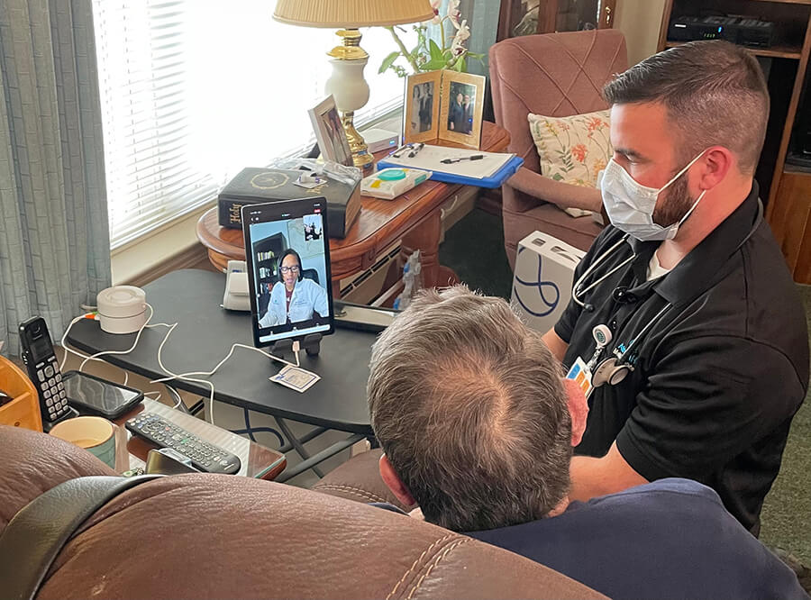 A medical professional and an older man sitting on a couch speaking with a doctor virtually.