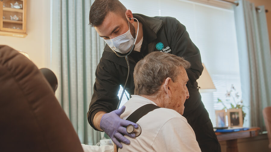 A medical professional checking the breathing of an older man.