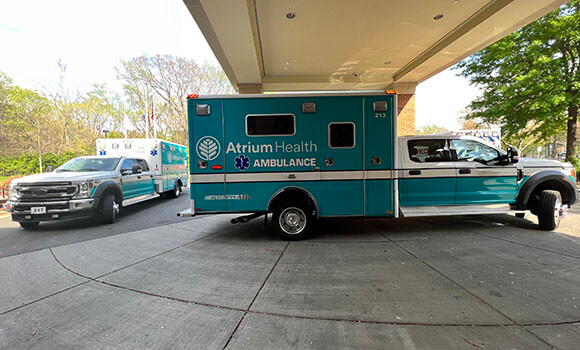 A teal and white ambulance parked under an overhang with a second one behind it to its left.