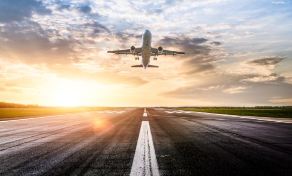 Commercial airplane flying off of runway with sunset behind.