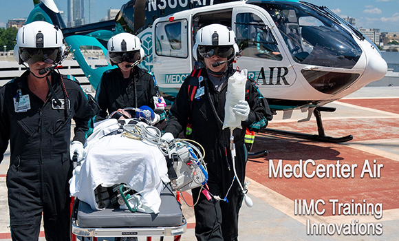 Three MedCenter air paremedics in flight uniforms and white helmets walk away from a helicopter while pushing a stretcher.