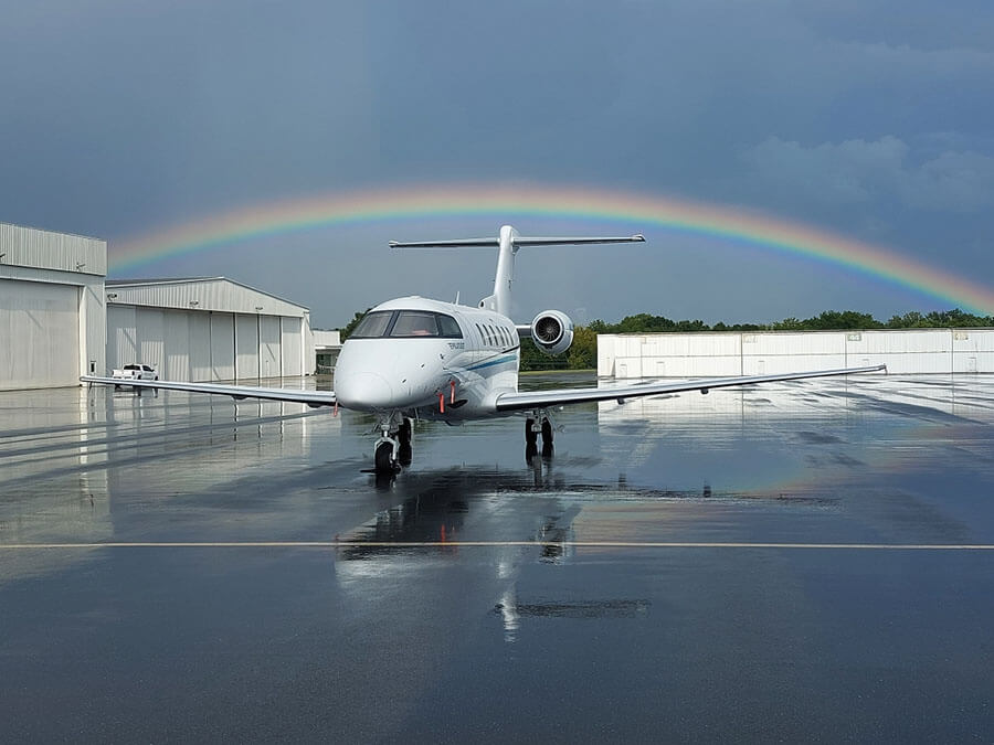 A small, fixed-wing plane outside on the tarmac with a rainbow in the background.