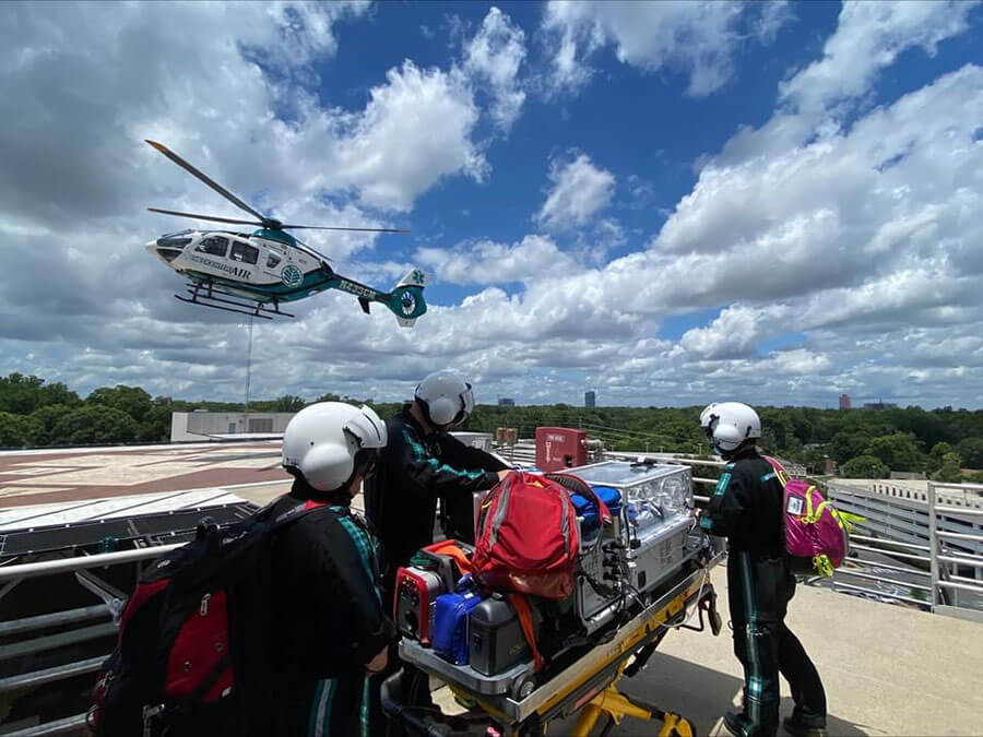 A group of medical personnel in flight suits await the arrival of a helicopter outside.