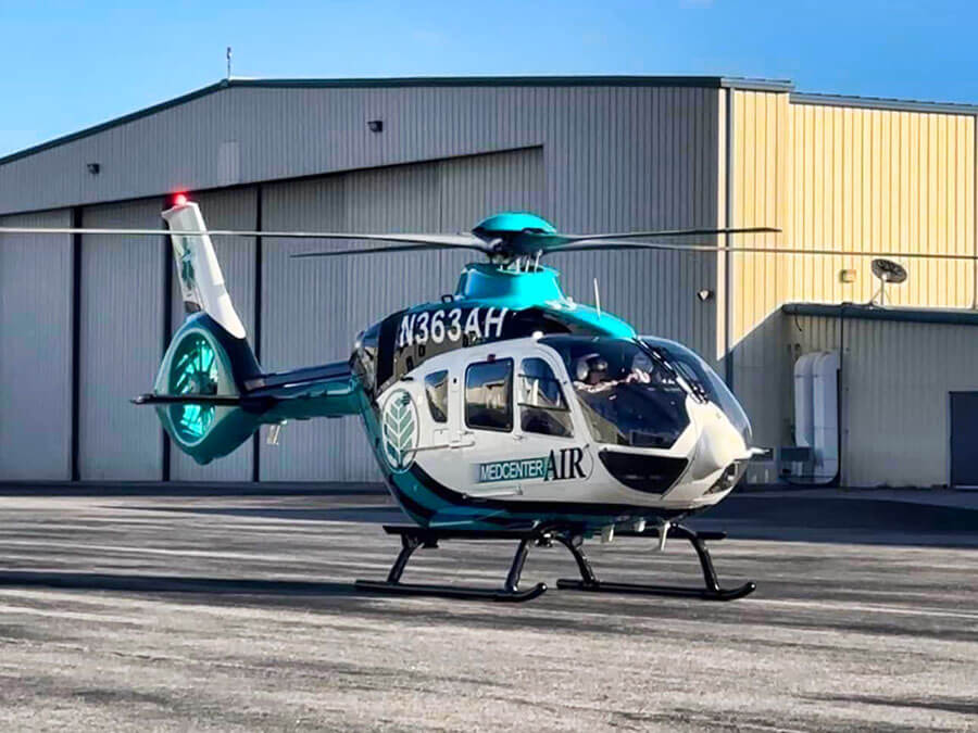 A teal, blue and white helicopter resting on the tarmac.